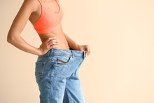 Beautiful Young Woman In Loose Jeans On Color Background. Weight Loss Concept