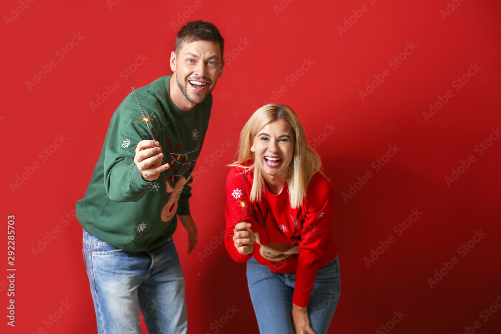 Happy couple with Christmas sparklers on color background