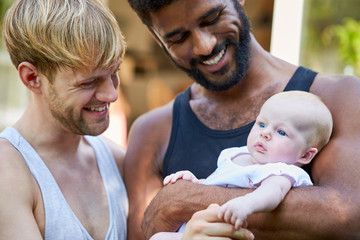 loving male same sex couple cuddling baby daughter at home in garden together