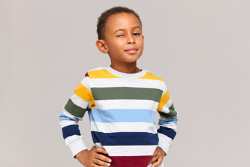 Poster - You know what am I saying? Positive confident playful Afro American little boy in multicolored sweater keeping hands on his waist and winking at camera. Human facial expressions and attitude