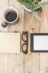 Still life view from above of new technology ebook beside a book and eyeglasses on a wooden table and a green aloe plant. New tech wireless device versus old traditional communication system.