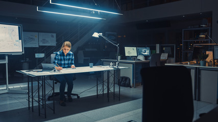 Poster - Female Engineer Sitting at Her Desk Works with Blueprints Laying on a Table, Uses Pencil, Ruler and Digital Tablet. In the Dark Industrial Design Engineering Facility