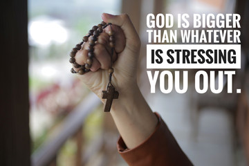 Inspirational quote - God is bigger than whatever is stressing you out. With young woman hand holding Rosary. with Jesus Christ Cross Crucifix. Month of Rosary, Christian Catholic religious symbol.