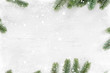 Pine leaves decorated as a frame on a white wooden background with snowflakes. Merry Christmas and winter holiday background.
