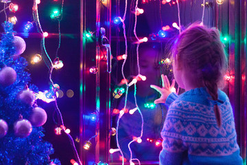 happy little cute, beautiful girl 5 years old is sitting on the window and playing with christmas li