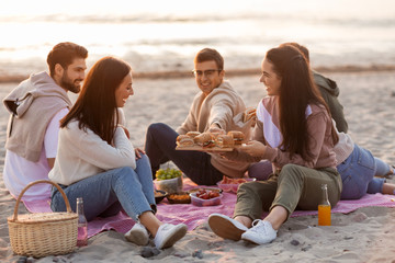 Sticker - friendship, leisure and fast food concept - group of happy friends eating sandwiches or burgers at picnic on beach in summer