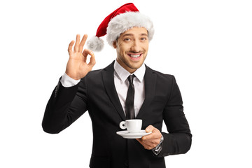 Wall Mural - Businessman with a Christmas hat holding a cup of espresso coffee and gesturing perfect