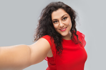 people and portrait concept - happy woman in red dress taking selfie over grey background