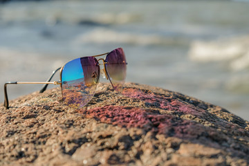 Reflection of the landscape in glasses. Colorful, sunglasses lie on a granite stone. Autumn, sunny day. Sea shore.