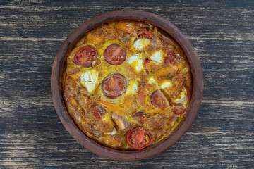 Ceramic bowl with vegetable frittata, simple vegetarian food. Frittata with tomato, pepper, onion and feta cheese on wooden table, close up. Italian egg omelette