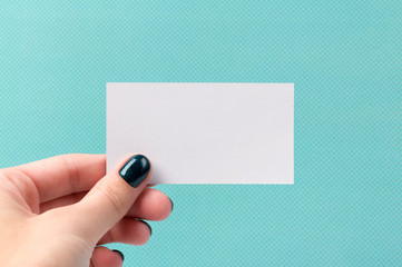 Manicured woman's hand holding business card on turquoise background