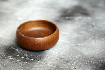 Wall Mural - One empty wooden bowl on grey background. Single round salad bowl on stone table with black paint stains, side view