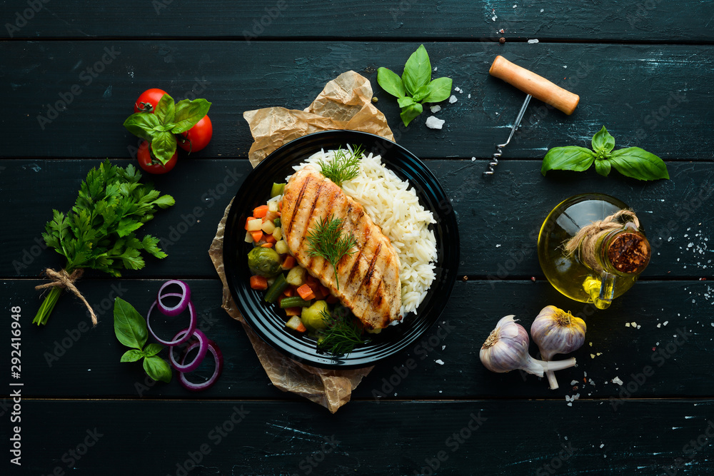 Baked chicken fillet with rice and vegetables on a black plate. Top ...