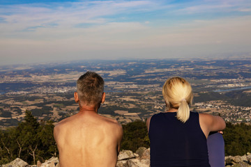 Happy white man and woman tourists  sitting  on edge of top of mountain and look into distance.