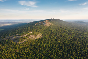 Panoramic aerial view of Ural mountains ridge with Pomyanenny (Kolchimsky) stone among taiga forest on a summer evening. Popular tourist place near Krasnovishersk, Perm krai, Russia.