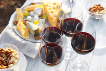 Red Wine And Snacks Served For Picnic On White Wooden Table Outdoors
