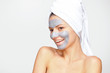 © volkonskaya - Beautiful young woman with a gray cosmetic mask on her face and a white towel on her head with bare shoulders.