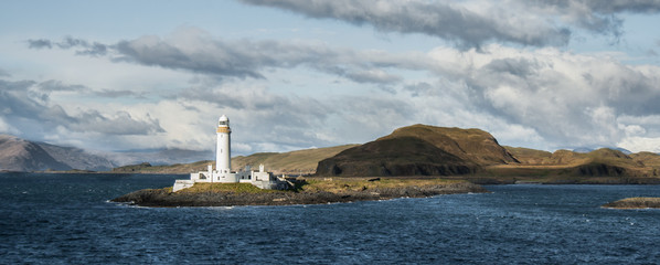 Eilean Musdile Lighthouse lit by the sun, in the West Coast of Scotland, seen from the ferry from Oban to Craignure, in the Isle of Mull. Seascape