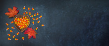 Heart Shaped Bowl Of Love Of Autumn Fall Halloween Candy Corn Spilled On Black Slate With Fall Autumn Leaves