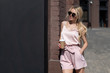 © Денис Бухлаев - beautiful blonde girl holds glass coffee in her hand and stands near an office brick building during break. Copy space for coffee shop advertisement