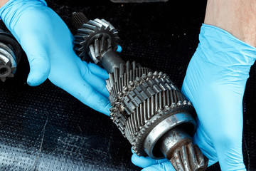 Wall Mural - Hands of a repairman in blue gloves hold gears, close-up. Repair box predach, repair of used cars. Metal background.