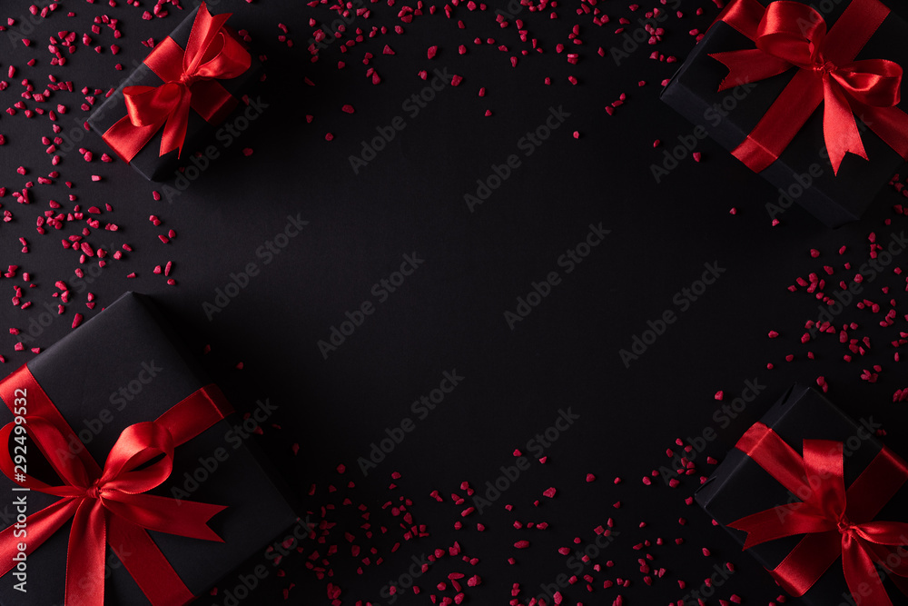 Top view of black christmas boxes with red ribbon on black background with copy space for text. black Friday composition. - obrazy, fototapety, plakaty 
