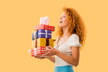 happy redhead girl holding gifts isolated on yellow