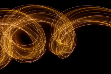 Wall Mural - Long exposure photograph of metallic gold neon colour in an abstract swirl, parallel lines pattern against a black background. Light painting photography.
