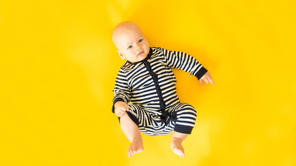 Calm curious baby lying on yellow background, looking at camera, top view, copy space