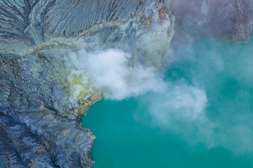 Aerial view of rock cliff at Kawah Ijen volcano with turquoise sulfur water lake at sunrise. Panoramic view at East Java, Indonesia. Natural landscape background.