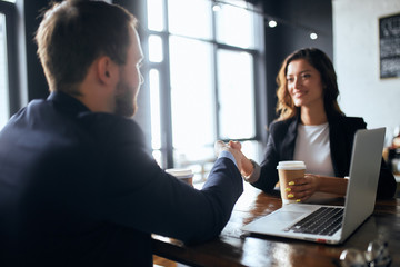 Wall Mural - cheerful brunette woman and brow-haired bearded man shaking hands during business meeting. close up photo