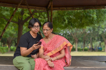 Wall Mural - Senior Indian mother with daughter learning mobile phone in a park in Delhi, India