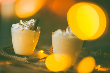 Eggnog in glasses with whipped cream and cinnamon on wooden table for Christmas and winter holidays. Copyspace included.