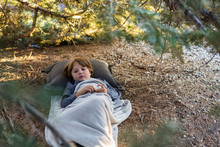 6 Year Old Boy Lying Down On Pine Needles Under Large Pine Tree.
