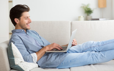 Canvas Print - Guy Working On Laptop Computer Lying On Sofa At Home