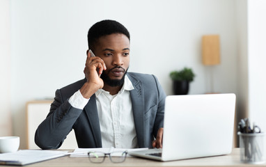 Poster - Focused afro businessman talking on cellphone and working on laptop