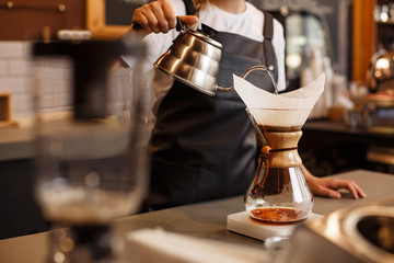 Professional barista preparing coffee using chemex pour over coffee maker and drip kettle. Young woman making coffee. Alternative ways of brewing coffee. Coffee shop concept.