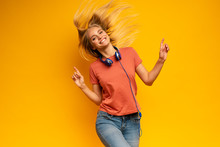 Blonde Girl Listens To Music With Headset. Joyful Expression On Yellow Background