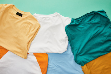 Wall Mural - top view of folded orange, beige, white, blue and ochre t-shirts on turquoise background