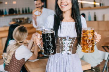 Wall Mural - cropped view of waitress in traditional german costume holding mugs of light and dark beer