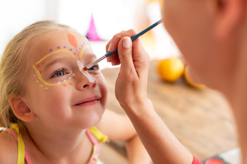 young mother painting daughters face for halloween party. halloween or carnival family lifestyle bac