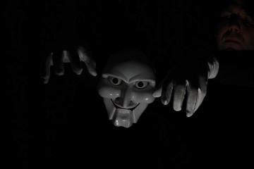 White scary mask on a black background with whites hand.