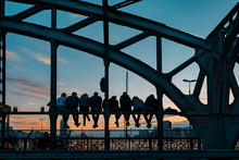 Backlight Of Several People Sitting Waiting For The Sunset On The Hacker Bridge Located In Munich