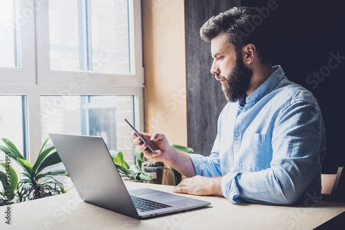 Fotomural Young man sitting in office and using laptop and smartphone for work