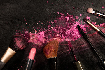 Wall Mural - Make-up brushes and lipstick with crushed cosmetics, overhead shot on a black background with copy space, a beauty design template for a makeup banner