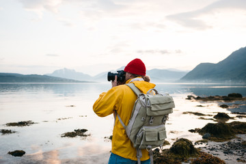 Wall Mural - Hipster traveler photographer takes a photo beautiful nordic landscape on professional camera. Man tourist with backpack shoots a photo scandinavia nature