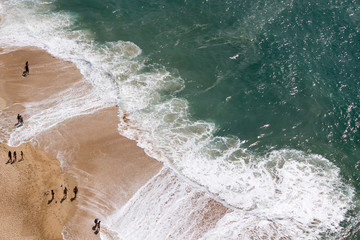 Drone view of people on the yellow sand beach facing the Beautiful crushing waves of Atlantic ocean in Nazare, Portugal	