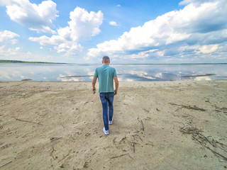 Wall Mural - Man is walking close up on the amazing background of the sea and reflection of the sky in water