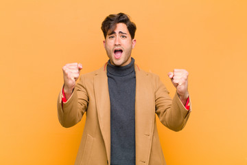 Wall Mural - young handsome man celebrating an unbelievable success like a winner, looking excited and happy saying take that! against orange background