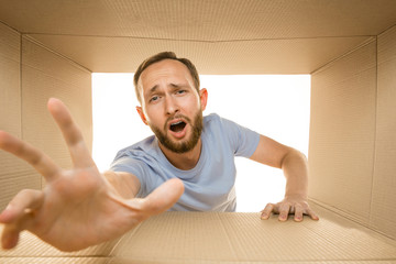 Young astonished man opening the biggest postal package isolated on white. Shocked male model on top of cardboard box looking inside. Gift, present, delivery, shipment, sales, black friday concept.